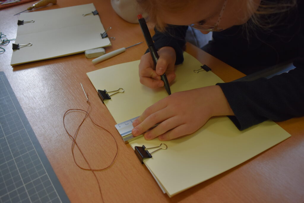 Kind bindet in Handarbeit mit Nadel und Faden ein selbst gefertigtes Heft.